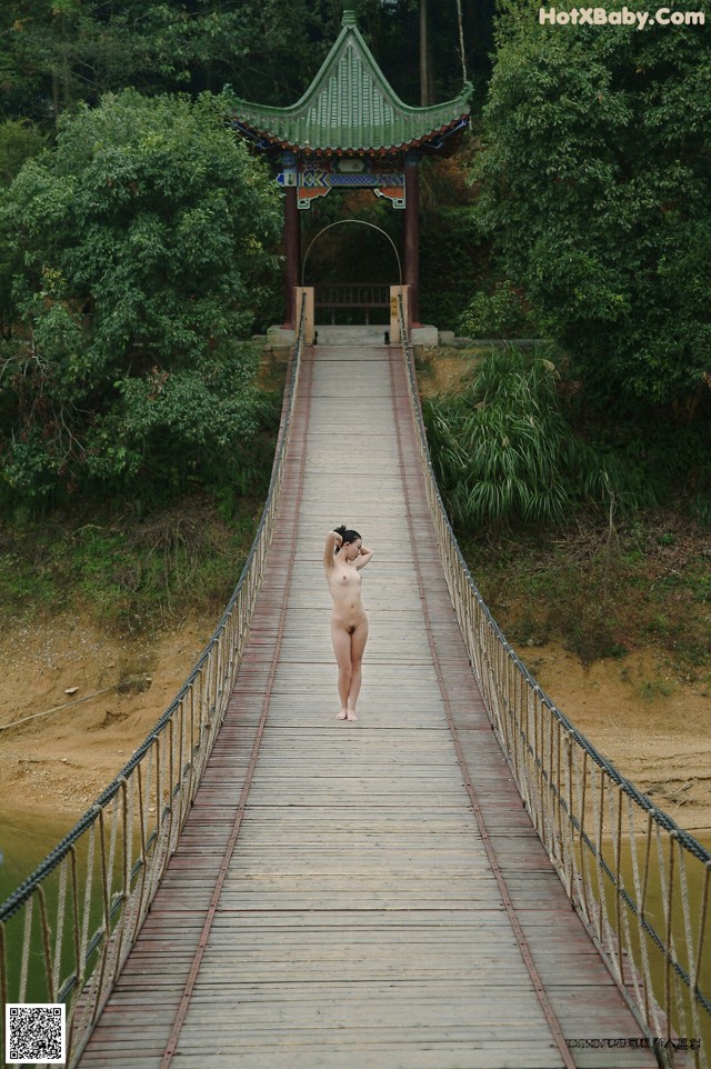 A naked woman standing on a wooden bridge.