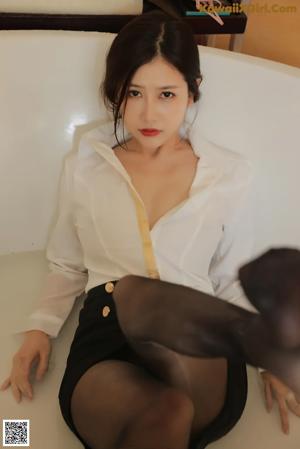 A woman in a white shirt and black skirt putting on a pair of white shoes.