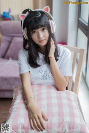 A woman sitting on a bed with a pillow and headphones on.