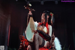 A woman in a red dress sitting on a chair holding a musical instrument.