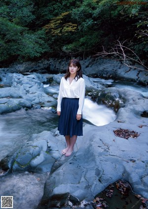 A woman in a white tank top and blue jeans posing on a couch.