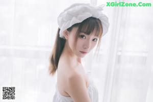 A woman in a white dress sitting on a bed.