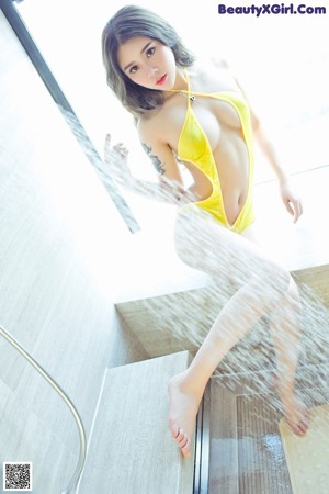 A woman in a yellow bathing suit sitting on a window sill.