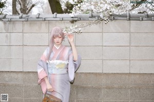 A woman in a kimono holding an umbrella in front of a tree.