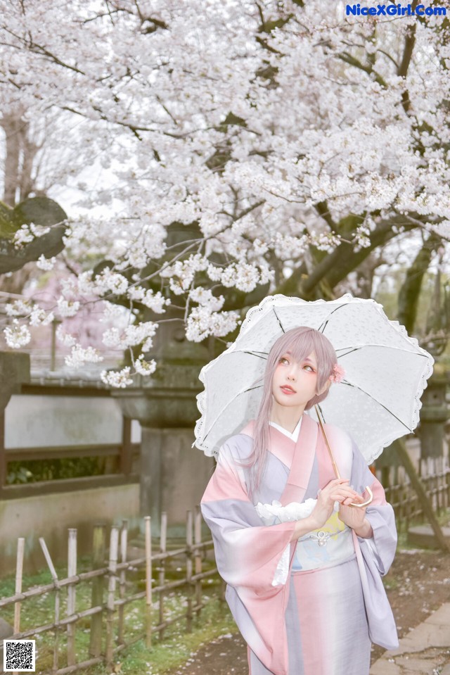 A woman in a kimono holding an umbrella in front of a tree.