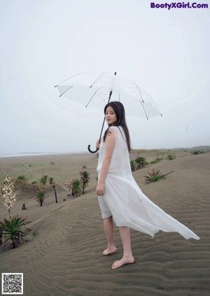 A woman with long black hair standing on a beach.