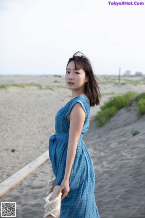 A woman in a blue dress posing on a beach.