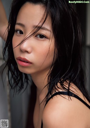 A woman in a black bra and panties leaning against a wall.