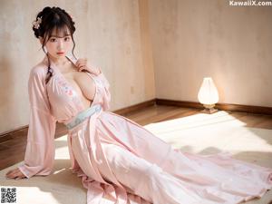 A woman in a pink dress sitting on a stone wall.