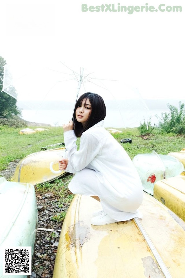 A woman sitting on top of a yellow canoe holding an umbrella.