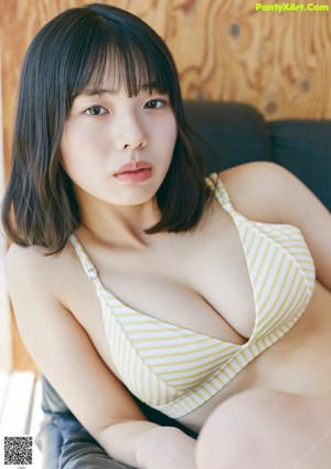 A woman in a yellow and white striped bikini sitting on a black couch.