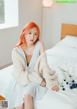 A woman with orange hair sitting on a couch wearing a hat.